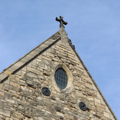 Gable end of the Greyfriars building with an oval shaped window and stone cross on the point of the roof.