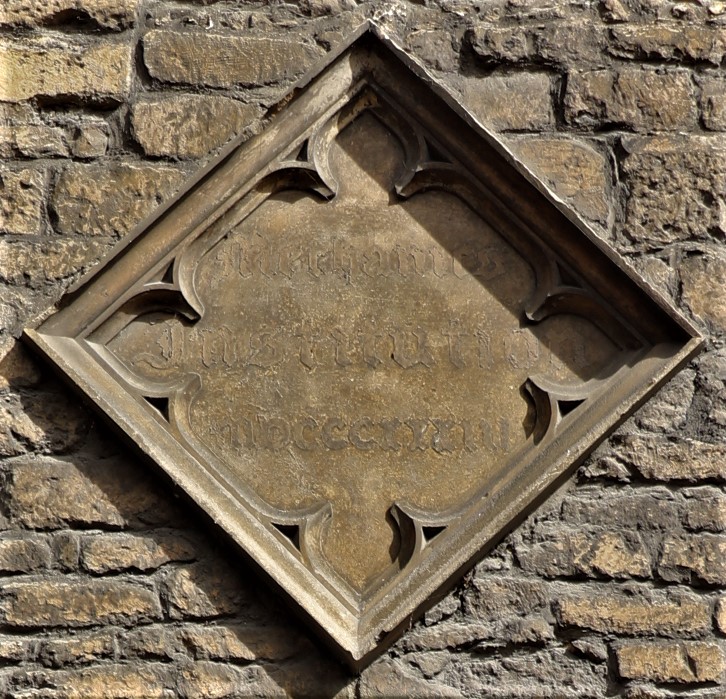 Close up of a diamond shaped stone plaque on a wall. Faint lettering says “Mechanics Institution mdcccxxxiii”