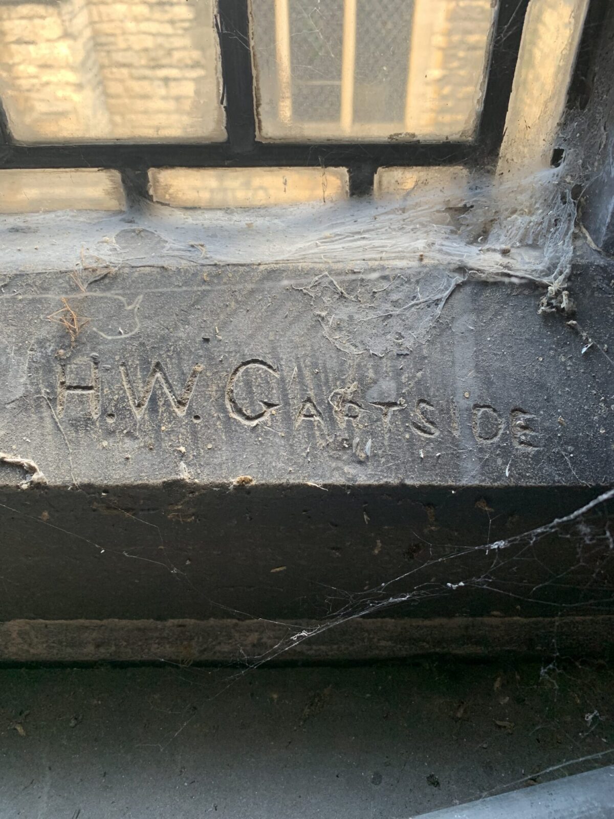 Close up of stone windowsill covered in cobwebs. Letters carved into the stone surface say “H.W.G. ARTSIDE”