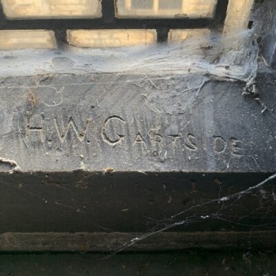 Close up of stone windowsill covered in cobwebs. Letters carved into the stone surface say “H.W.G. ARTSIDE”