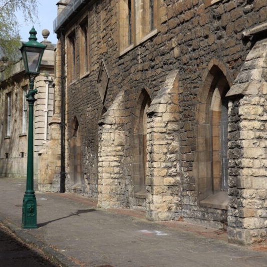 Exterior view of Greyfriars building showing buttresses and windows with an old-fashioned streetlight in the foreground.