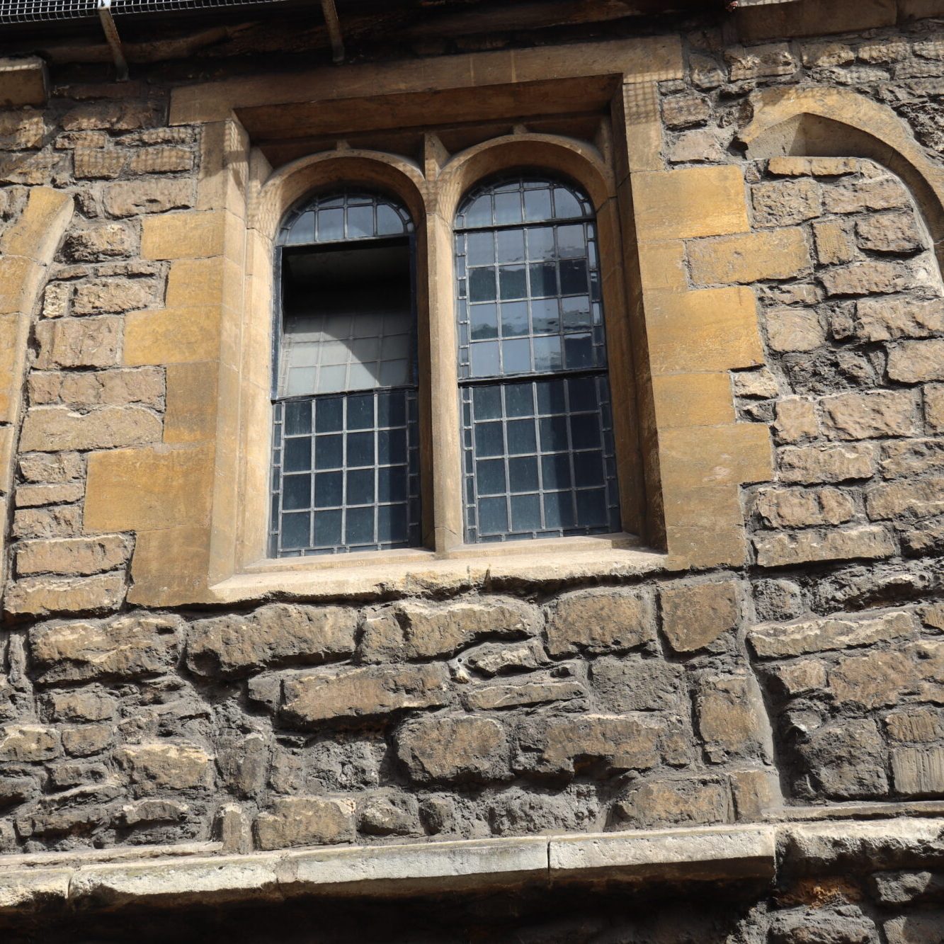 View of a window in a stone wall with masonry indicating where a larger window once sat in the wall.